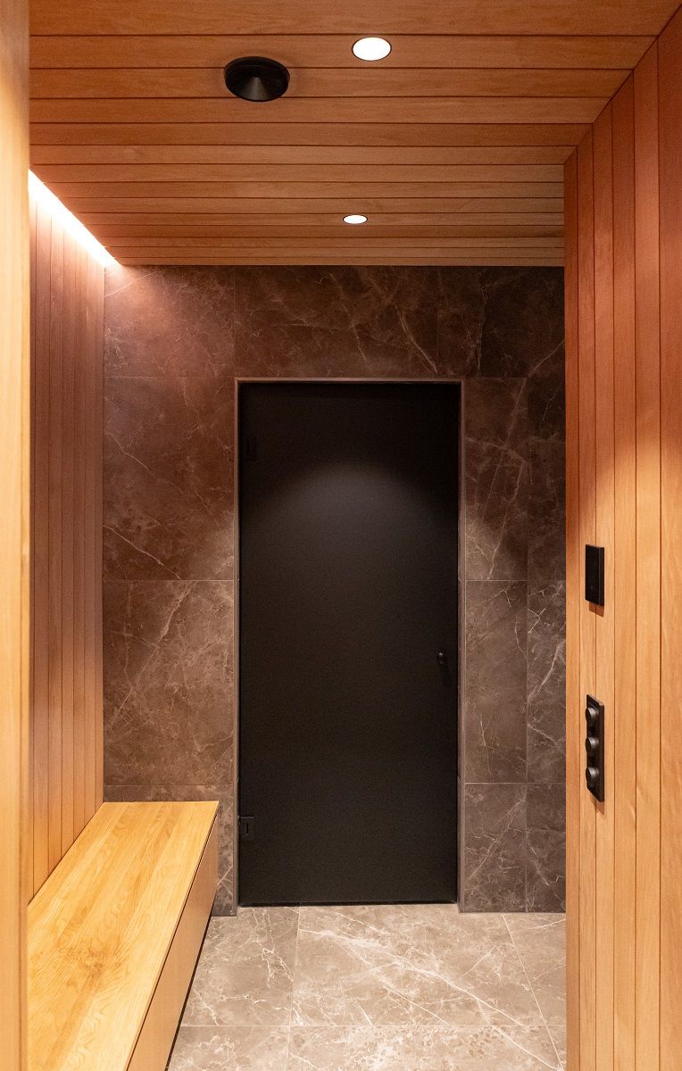 In the changing room corridor, recessed LED spotlights in the ceiling and indirect LED strip lighting above the bench at the ceiling border.
